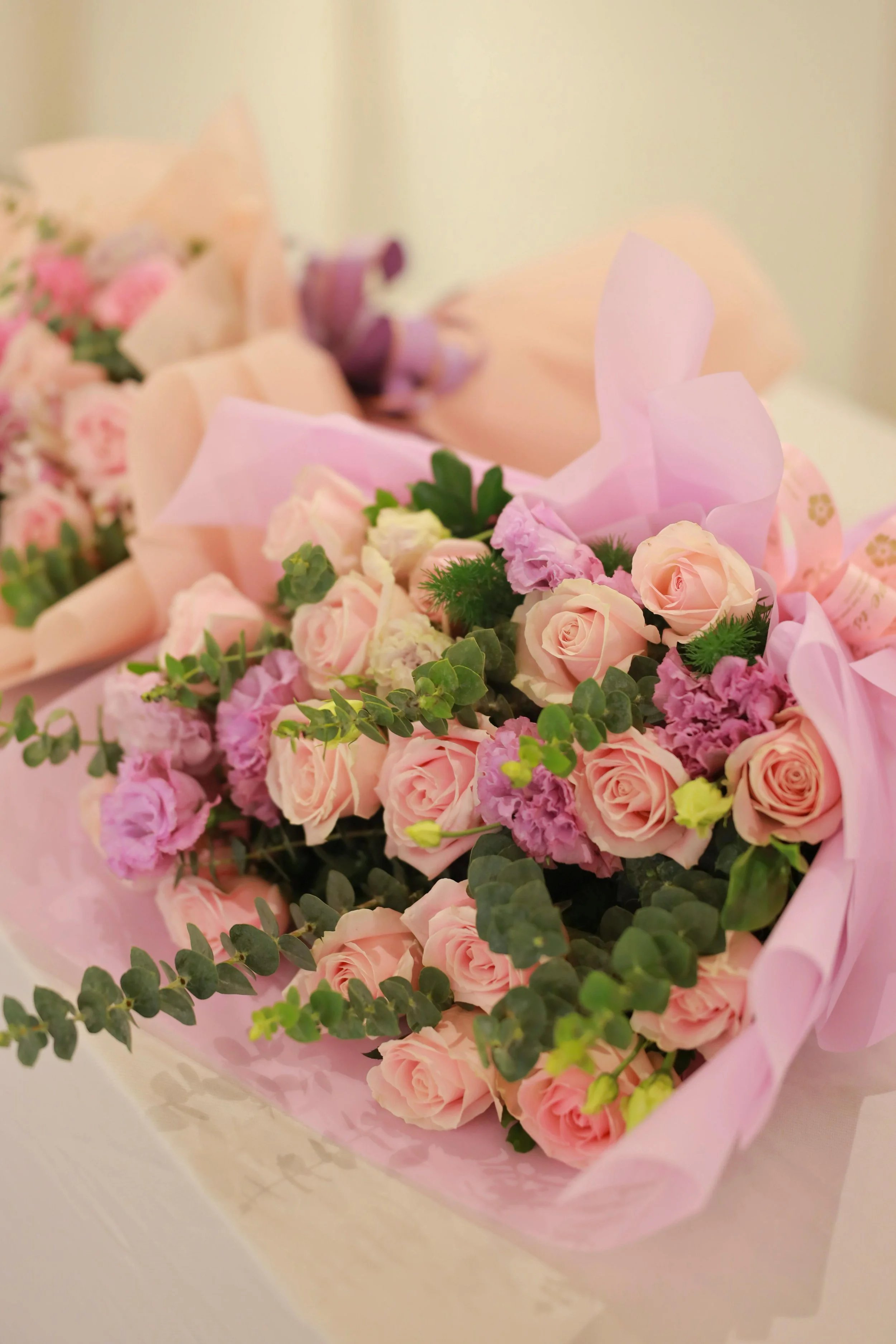 A bouquet of pink roses, purple flowers, and greenery wrapped in pink paper.