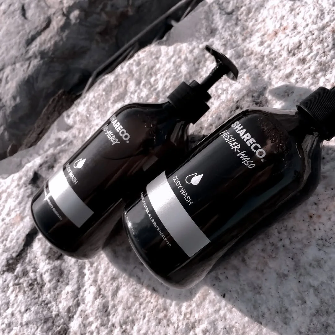 Two black bottles labeled 'SHARECO BODY WASH' and 'SHARECO HAIR & BODY WASH' placed on a rocky surface outdoors.