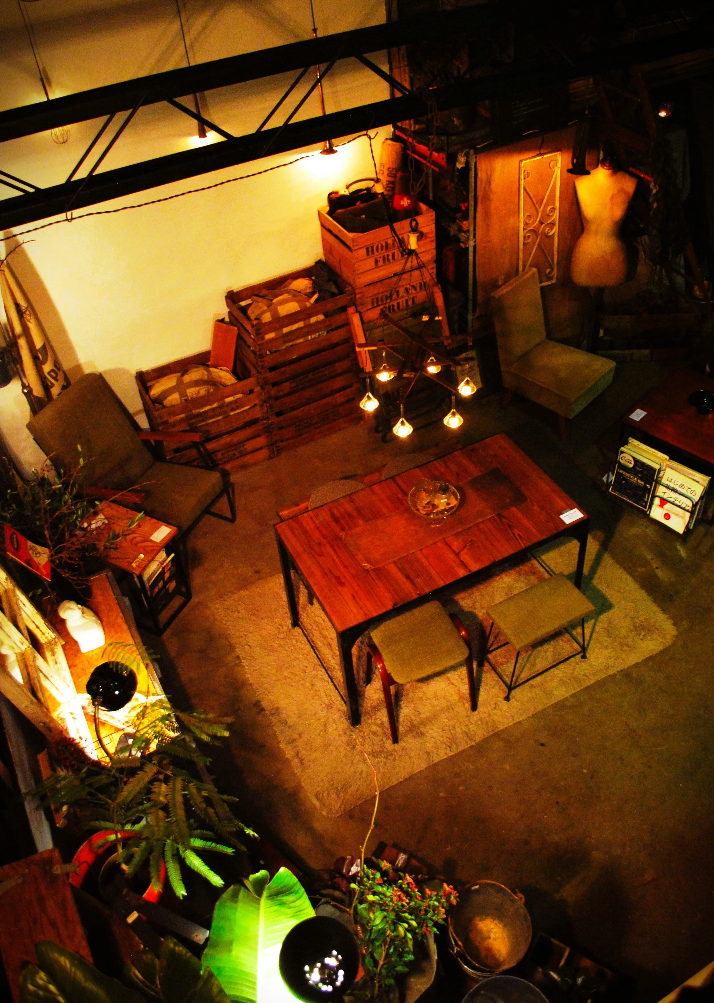 温かい照明と木製家具のリビングルームの室内風景。テーブル、椅子、植物、デコレーションなどが配置されている。