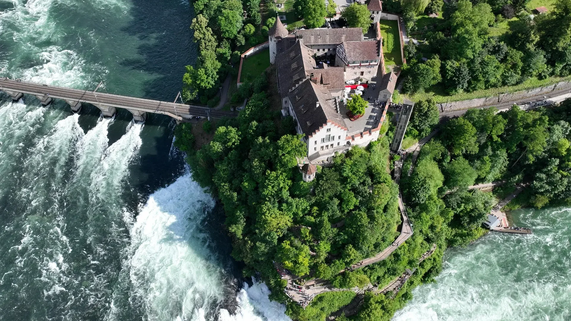 Vista aérea de Schloss Laufen sobre las cataratas del Rin, rodeado de bosque y agua