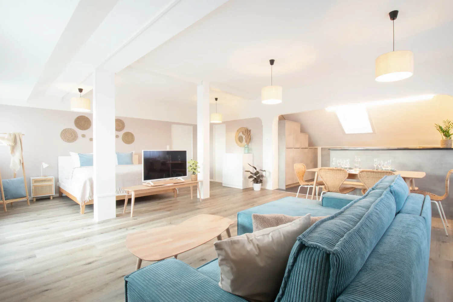 Lichtdurchflutetes Apartment Blau mit offenem Wohnbereich, blauer Couch und Blick auf Ess- und Schlafbereich