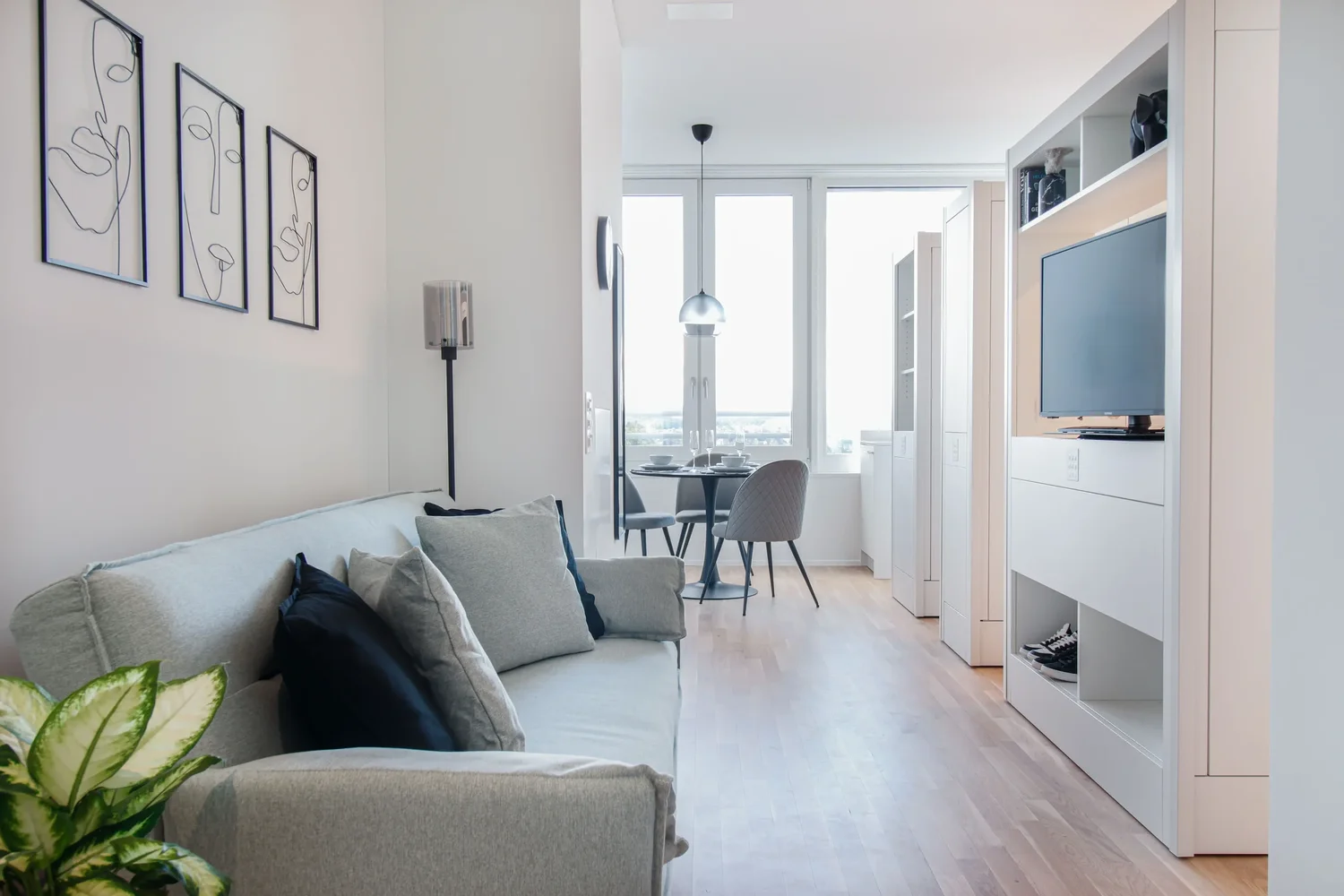 Wohnbereich im Apartment Grau mit grauem Sofa, moderner Wandkunst und hellem Essbereich am Fenster