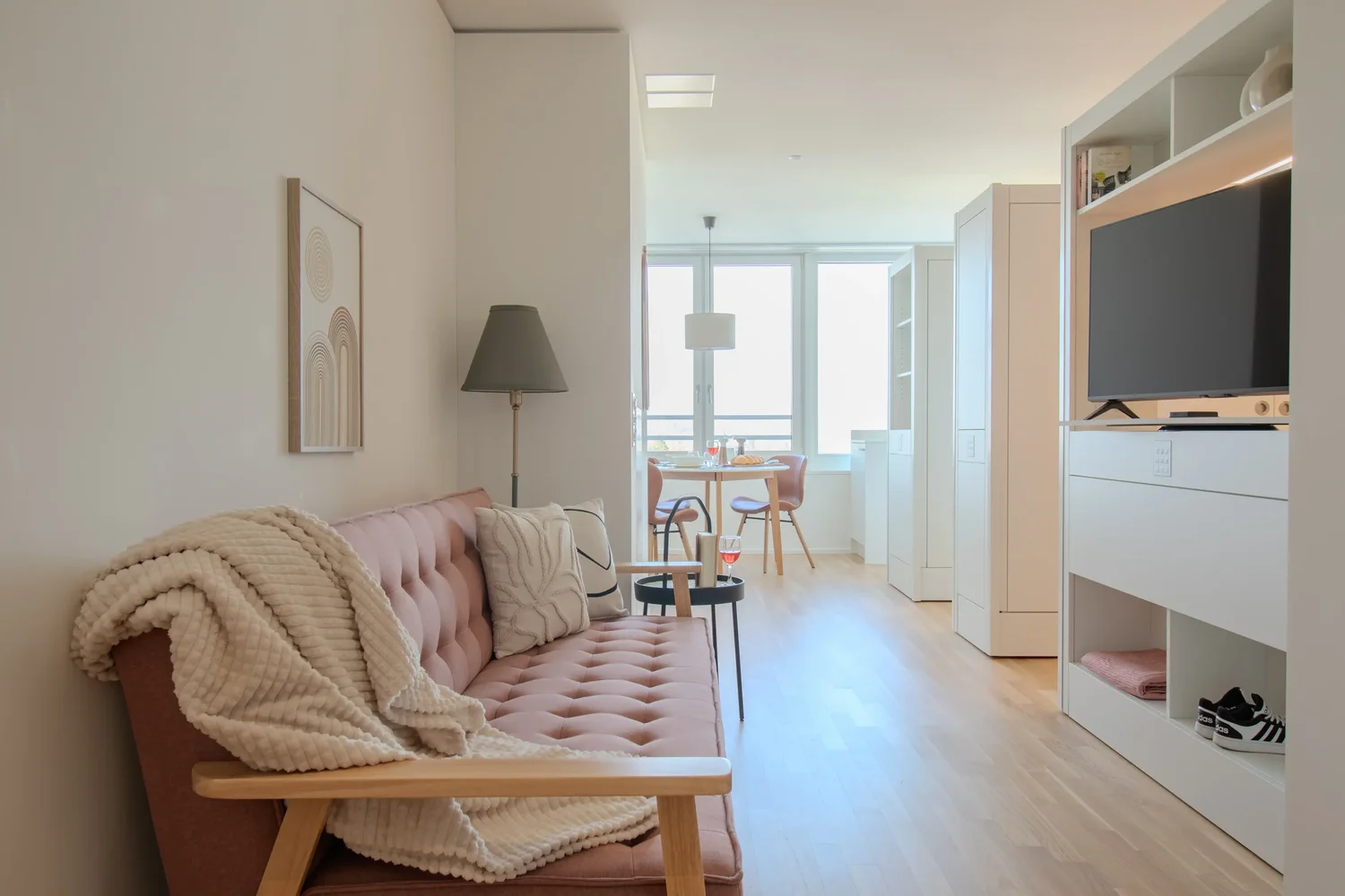 Wohnbereich im Apartment Coral mit Sofa, Essplatz am Fenster und hellem Holzfußboden