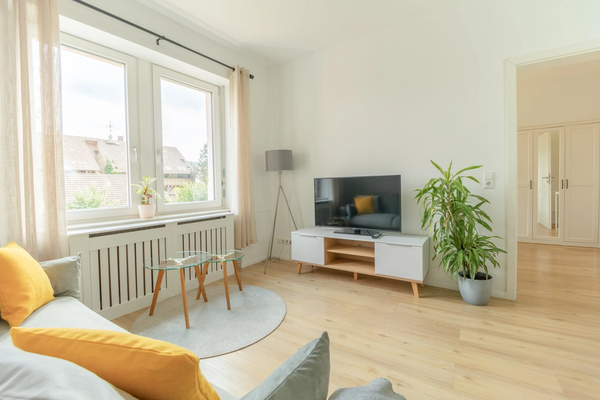 Lichtdurchflutetes Wohnzimmer mit TV-Bereich, gemütlichen Sitzmöglichkeiten und warmen Gelb-Akzenten – ideal zum Entspannen nach einem Tag in der Region.
