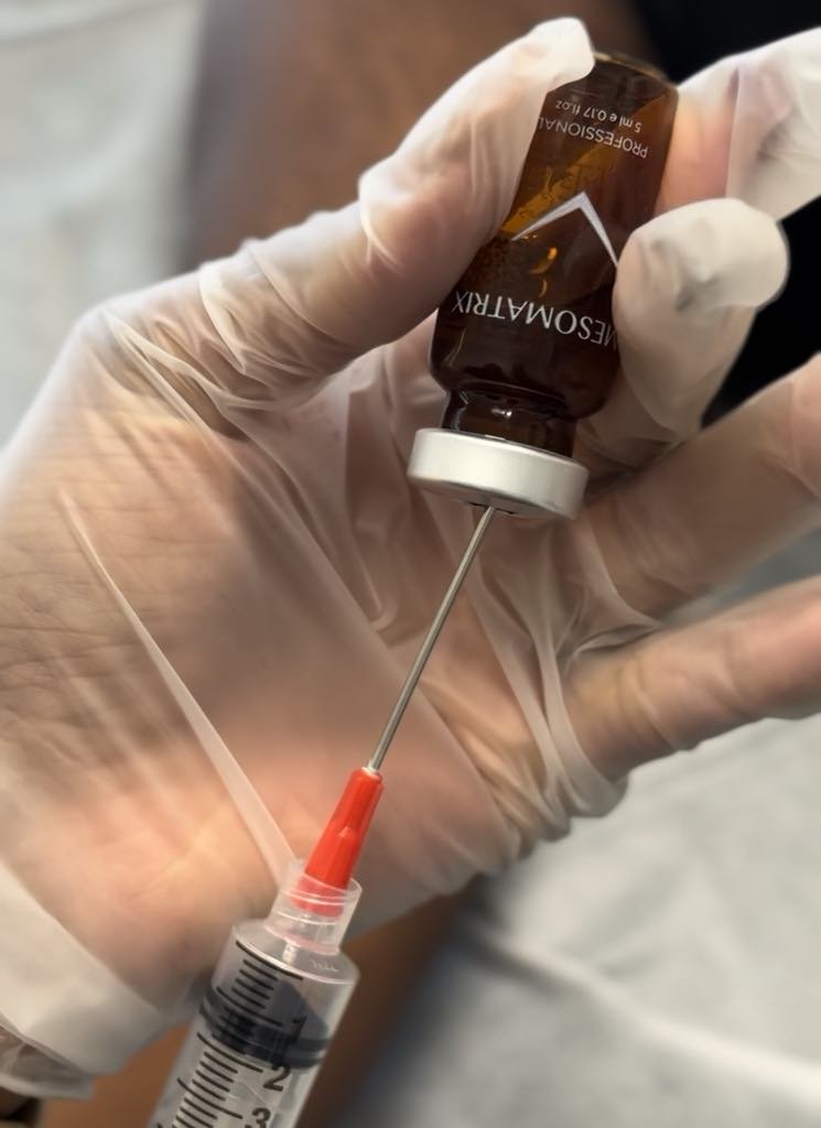 Une personne portant des gants en latex prépare une injection à partir d'une ampoule de médicament et d'une seringue.