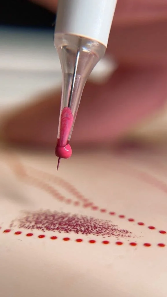 Une main tient une pipette déposant de petites gouttes de colorant rose pour créer un motif artistique sur une surface