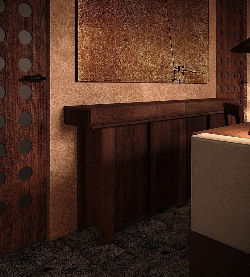 A dark wooden sideboard against a textured brown wall with an abstract art piece hanging above it. To the left, a door with circular cutouts, and to the right, a dining table with a chair partially visible. The floor is tiled.