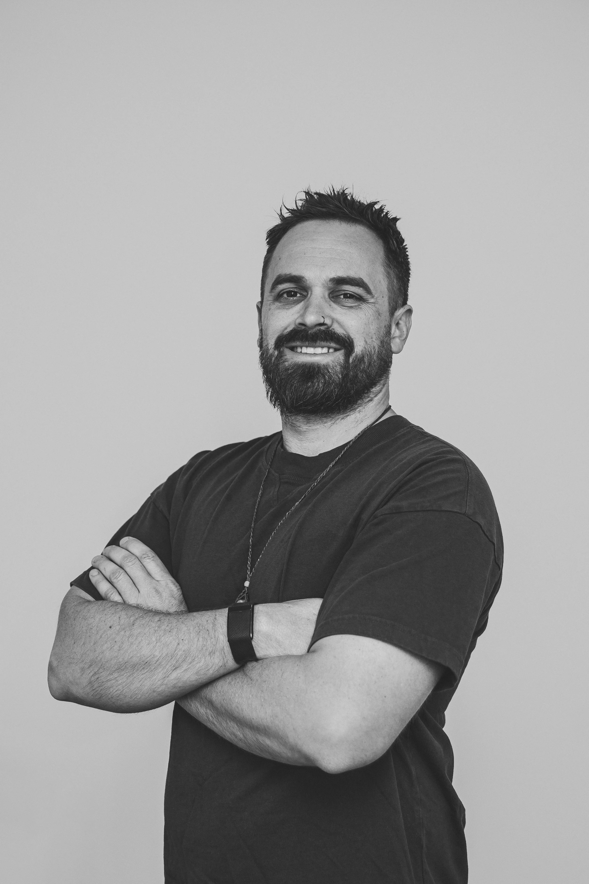 Black and white portrait of a man with a beard, crossing his arms and smiling, against a plain background.