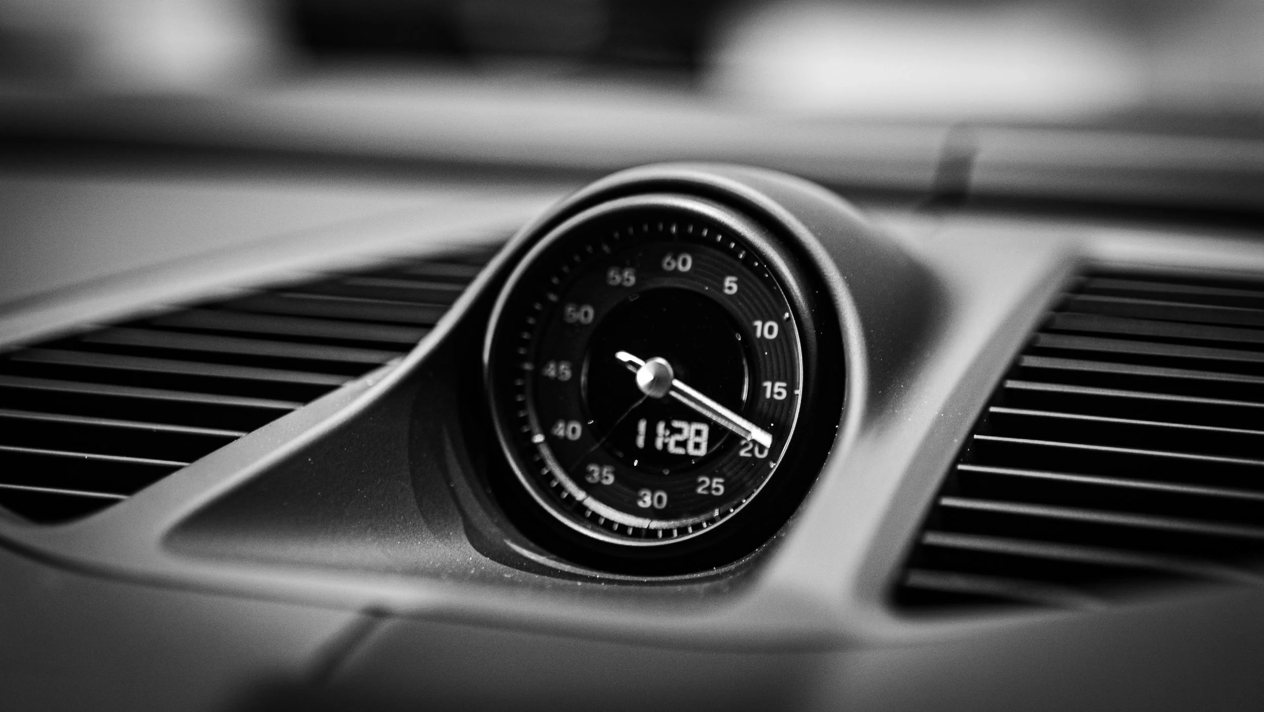 Close-up of a car's analog clock and digital clock display on the dashboard in black and white.