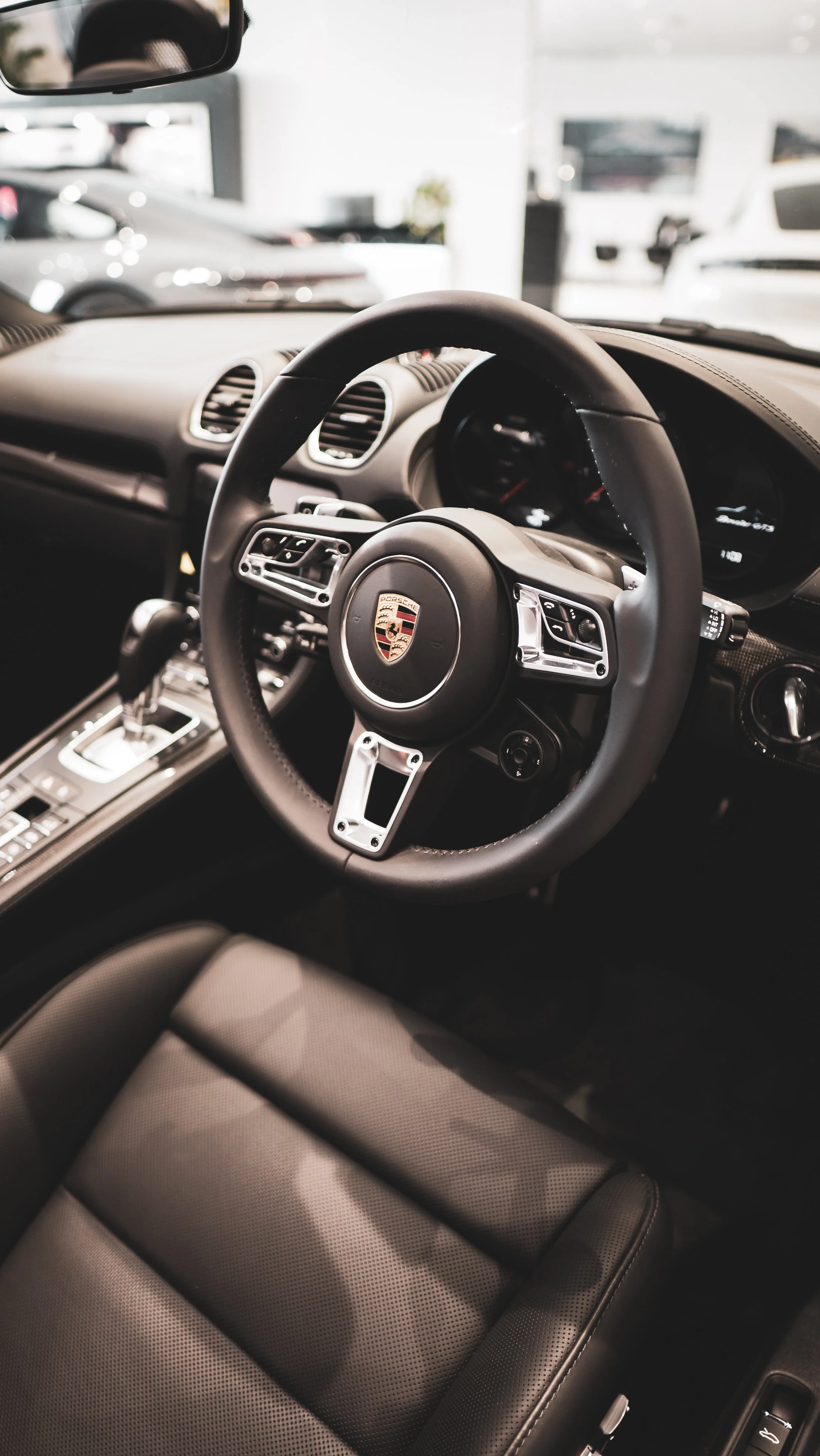Interior of a Porsche sports car, showing the steering wheel with the Porsche logo, gear shift, and dashboard.