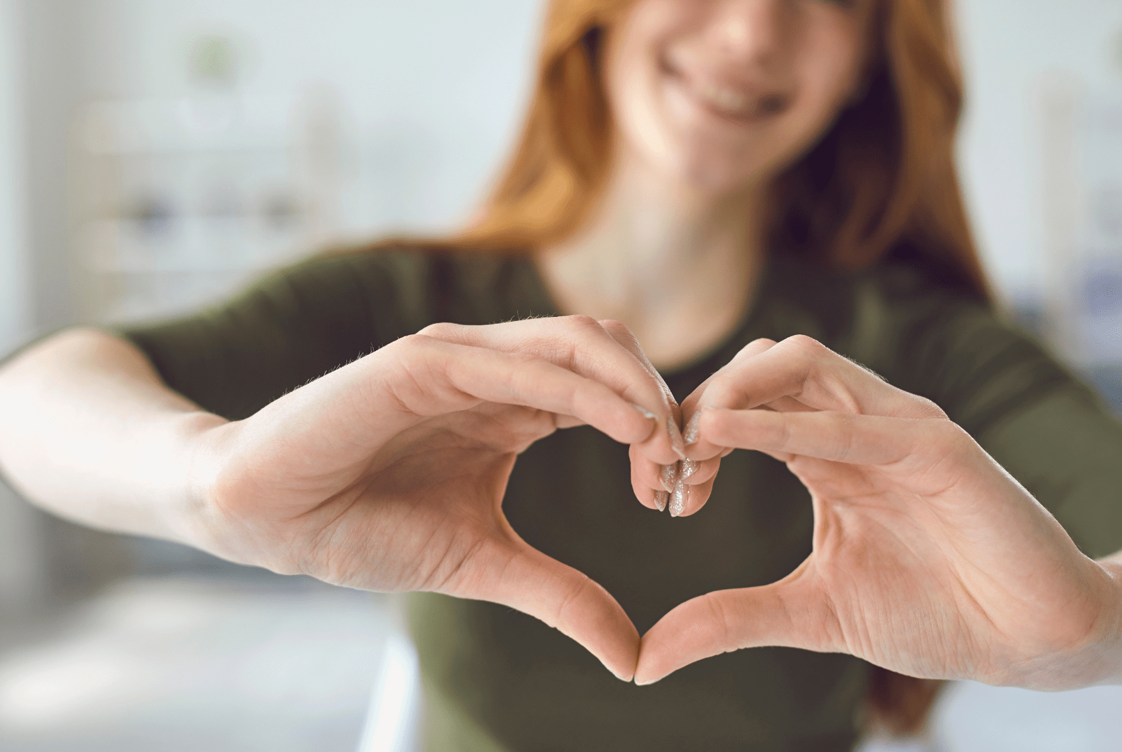 A woman with red hair making a heart shape with her hands.