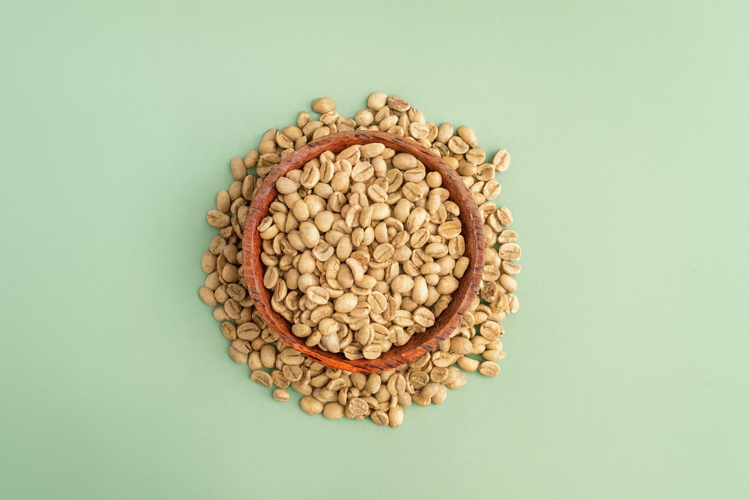 Raw green coffee beans in a wooden bowl on a green background.