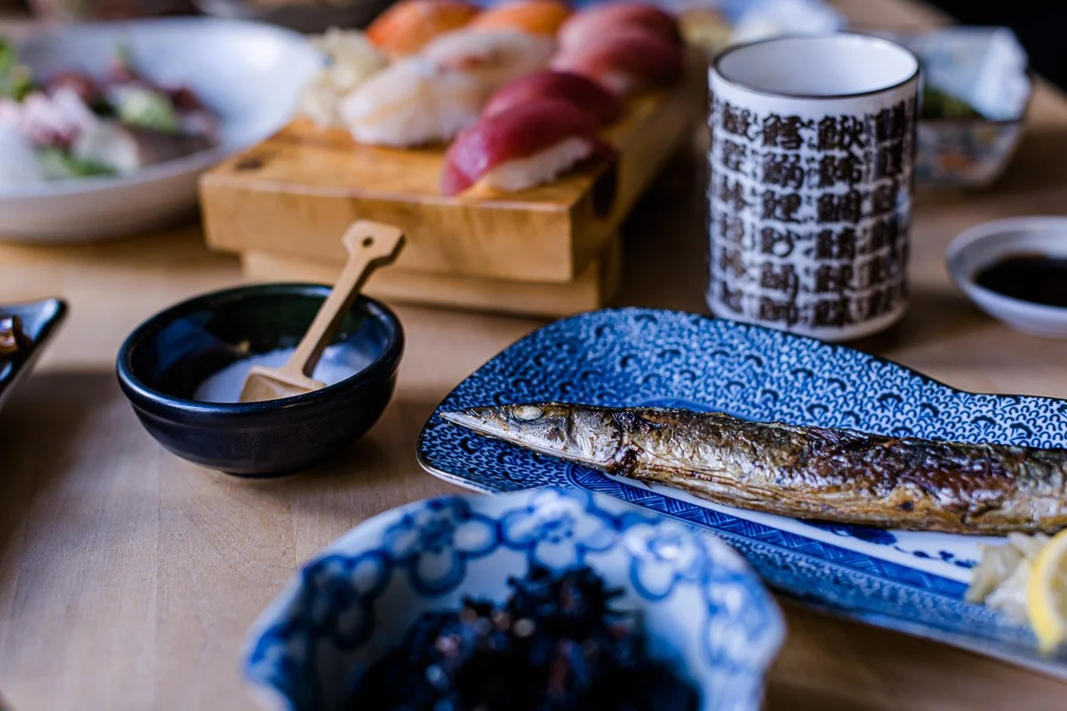 Gericht mit gegrilltem Fisch, Sushi, Sojasauce, Wasabi und anderen japanischen Speisen auf einem Tisch.