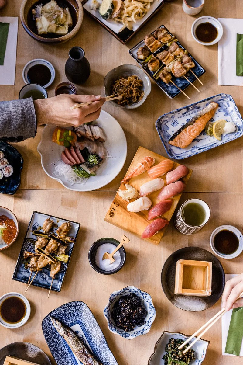 Ein japanisches Sushi-Essen mit verschiedenen Sushi-Variationen, gegrilltem Fisch, japanischen Beilagen und Sojasaucen auf einem Holztisch.