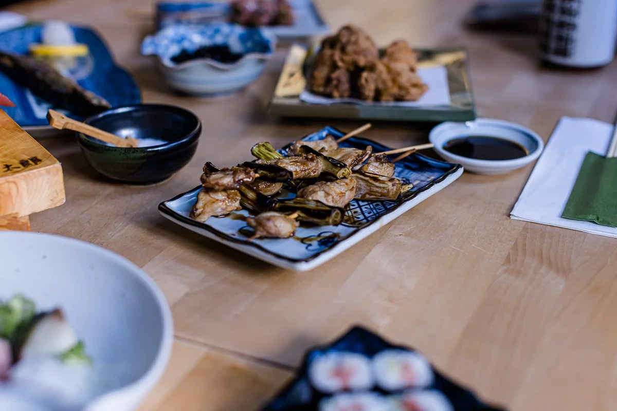 Japanisches Essen auf einem Holztisch mit verschiedenen Gerichten, einschließlich gegrilltem Fleisch mit Frühlingszwiebeln und Soja-Sauce.