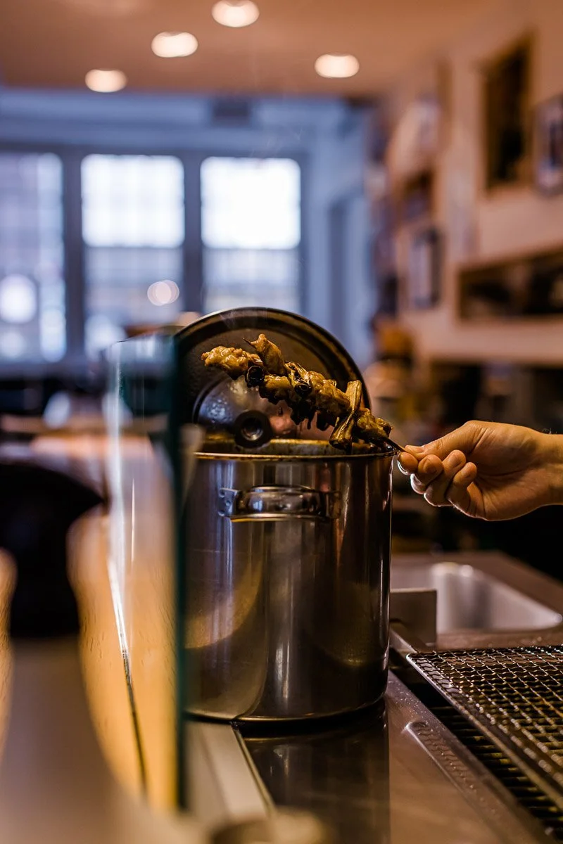 Eine Hand, die einen Fleischspieß aus einem mit warmem Licht beleuchteten Gasgrill nimmt.