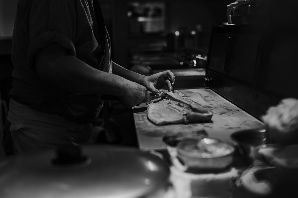 Person schneidet Fisch in einer dunklen Küche.