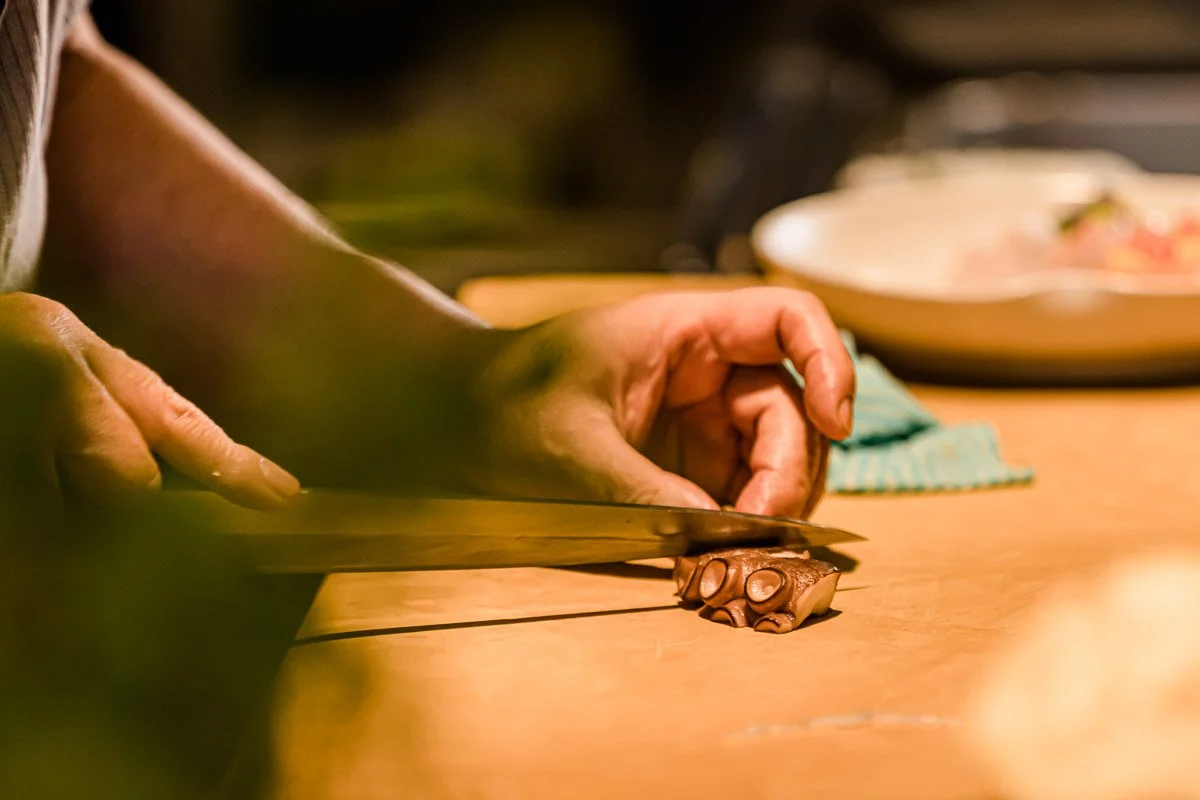 Person schneidet Schokolade auf einem Holztisch mit einem Messer.