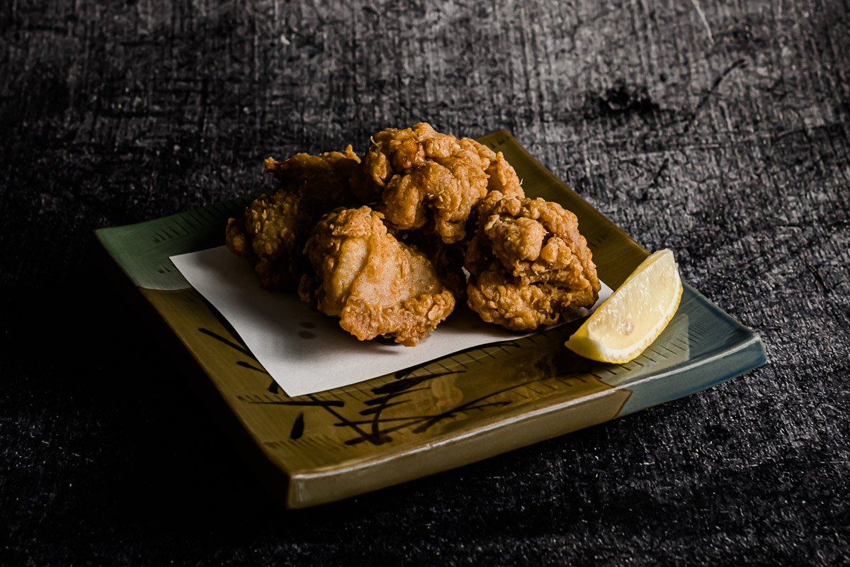 Frittierte Hähnchenteile mit Zitronensaft auf einem dekorativen Teller auf schwarzem Hintergrund.