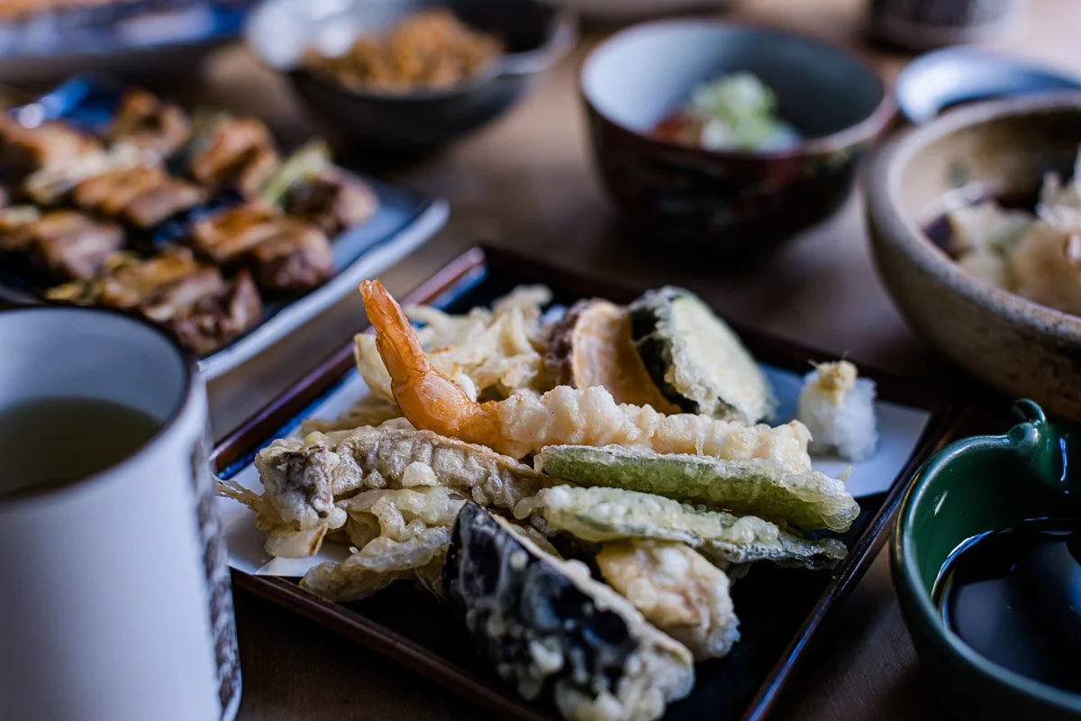Verschiedene japanische Gerichte, darunter Tempura mit Garnelen und Gemüse, auf einem Tisch.