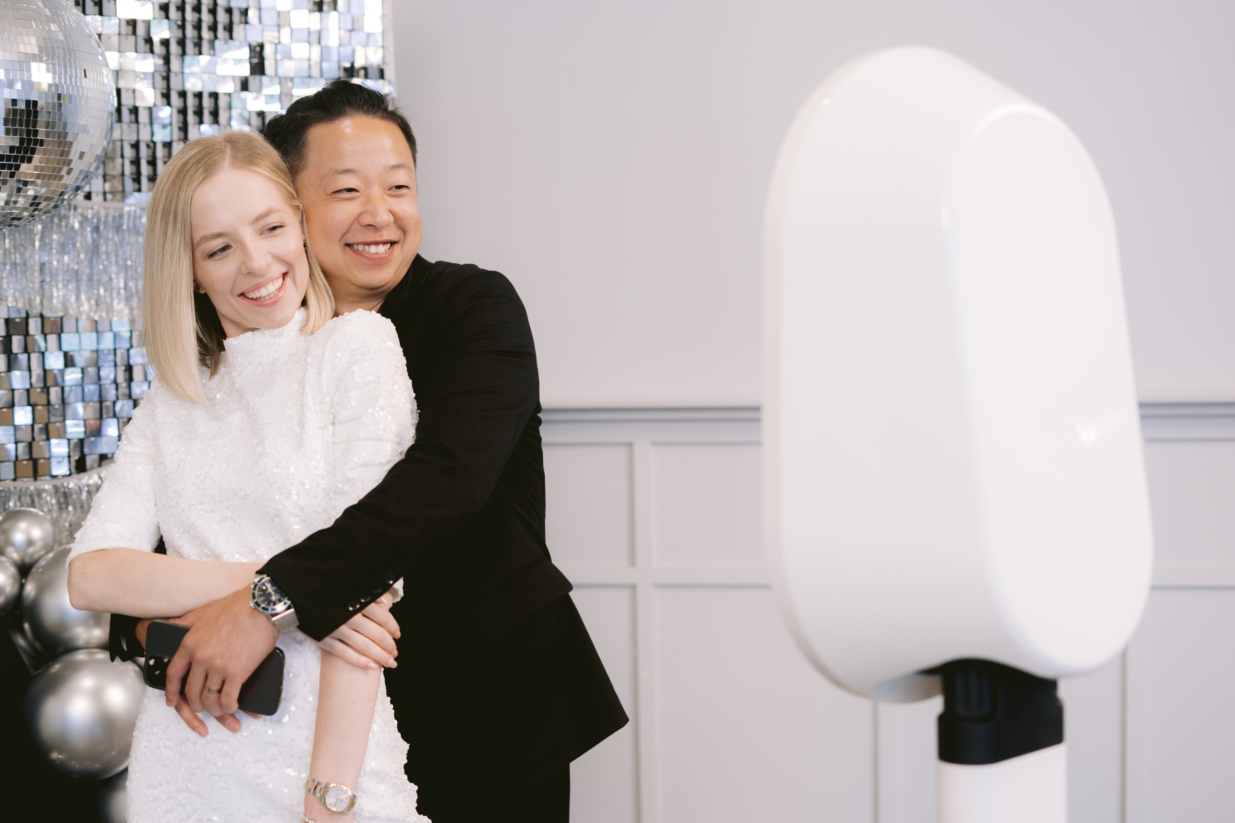 Couple hugging in front of a white elegant photobooth setup