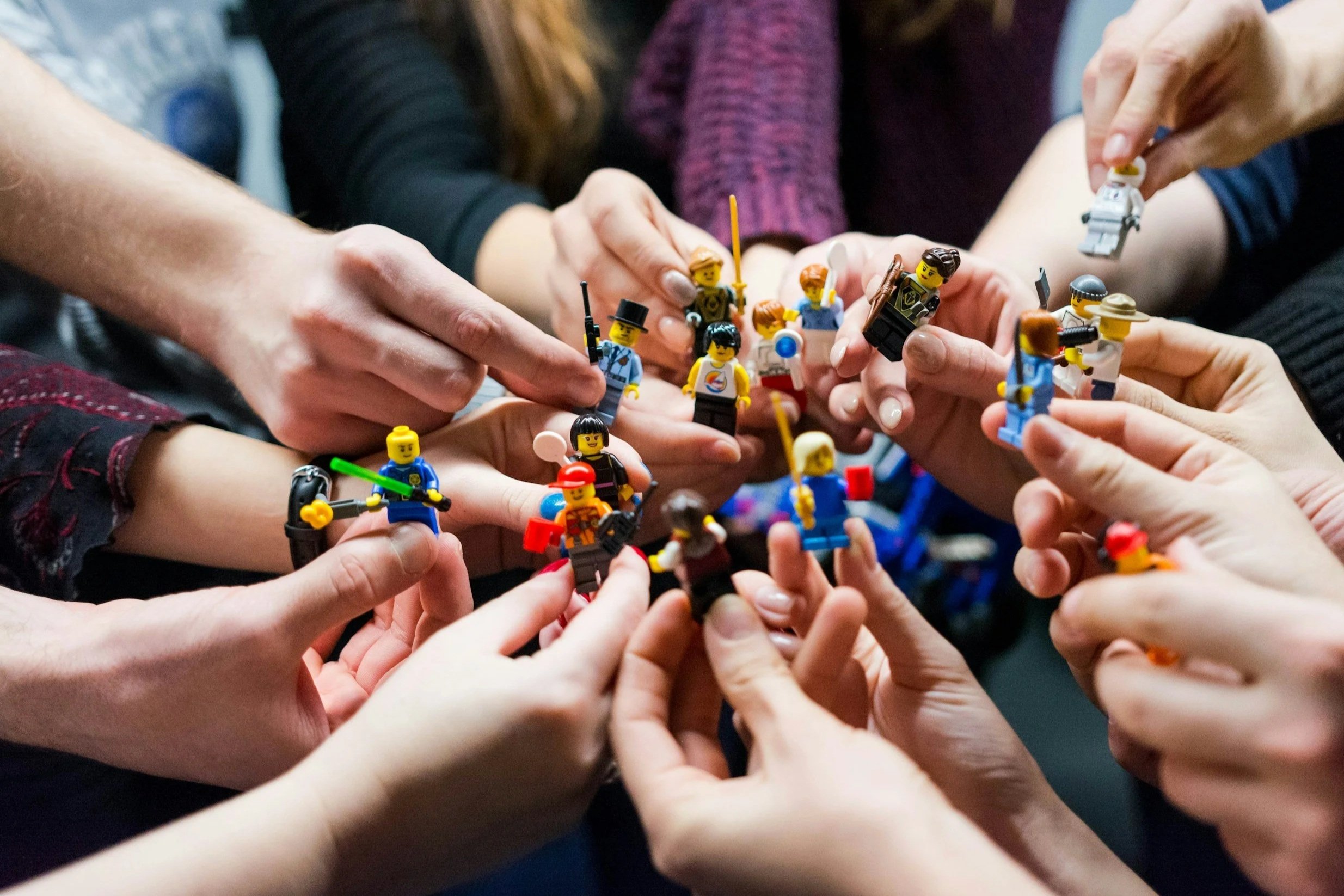 LEGO vinnustofa, teymisþjálfun og hópefli.. Multiple people holding and assembling LEGO minifigures closely together in a workplace setting