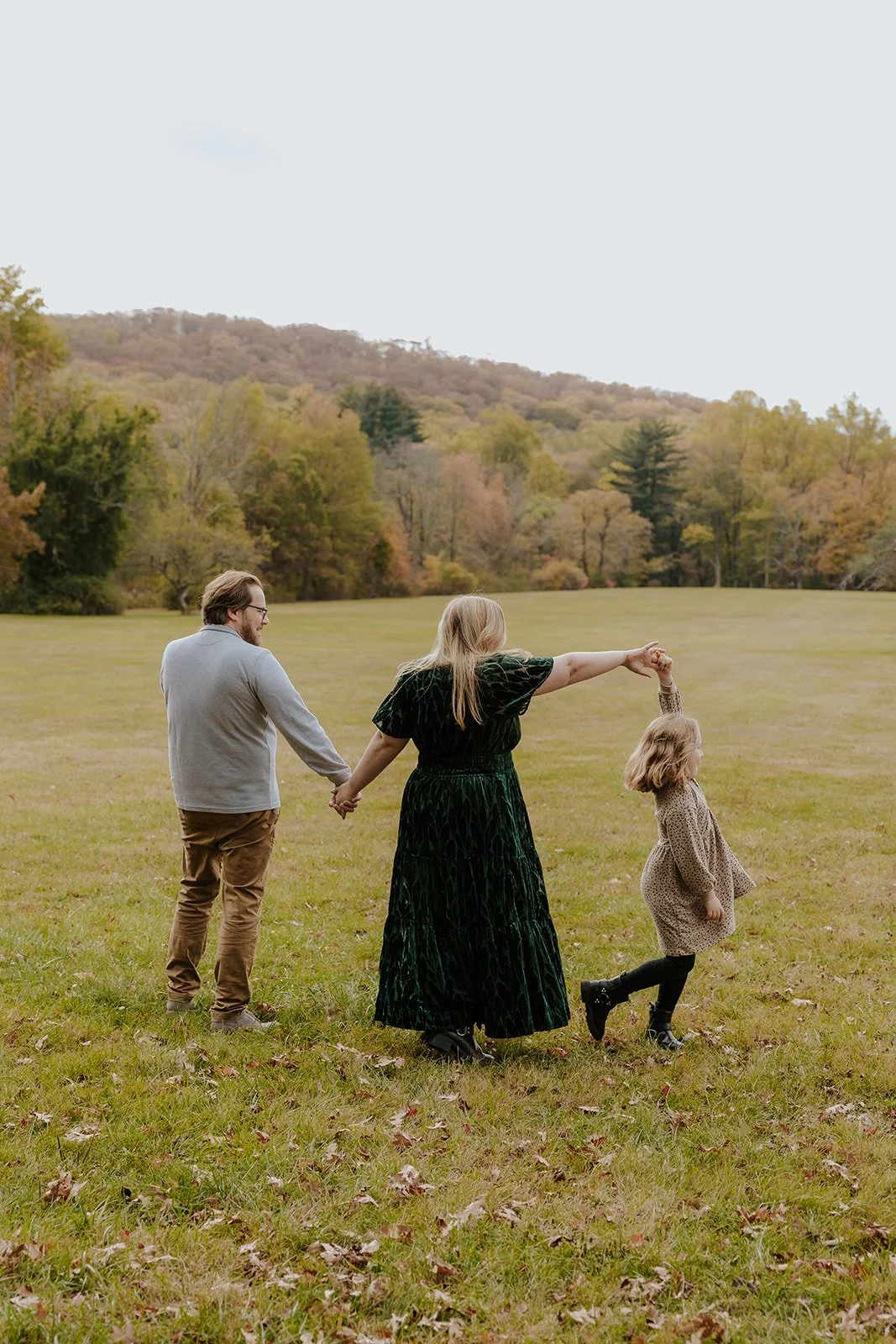 Pictures  family of three holding hands and playing in a grassy field during autumn at the New Jersey botanical garden