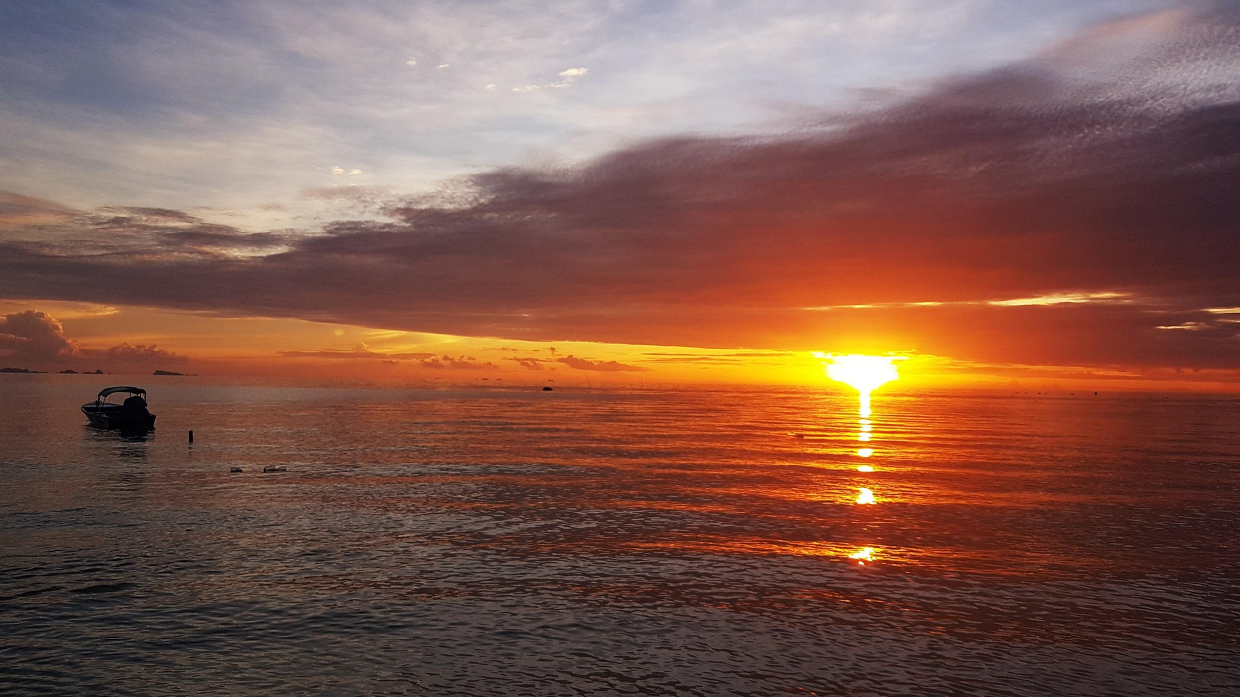 Coucher de soleil sur une mer calme, bateau à l'horizon