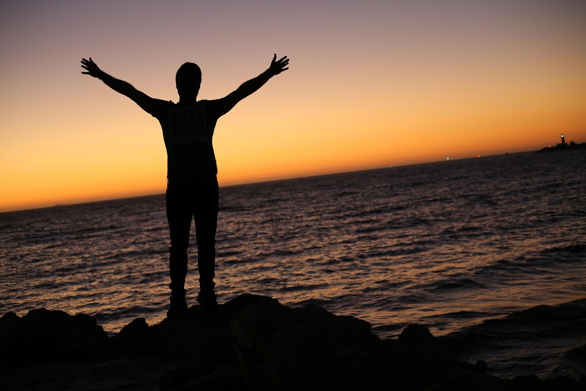 Silhouette d'une personne bras ouverts face à la mer au crépuscule