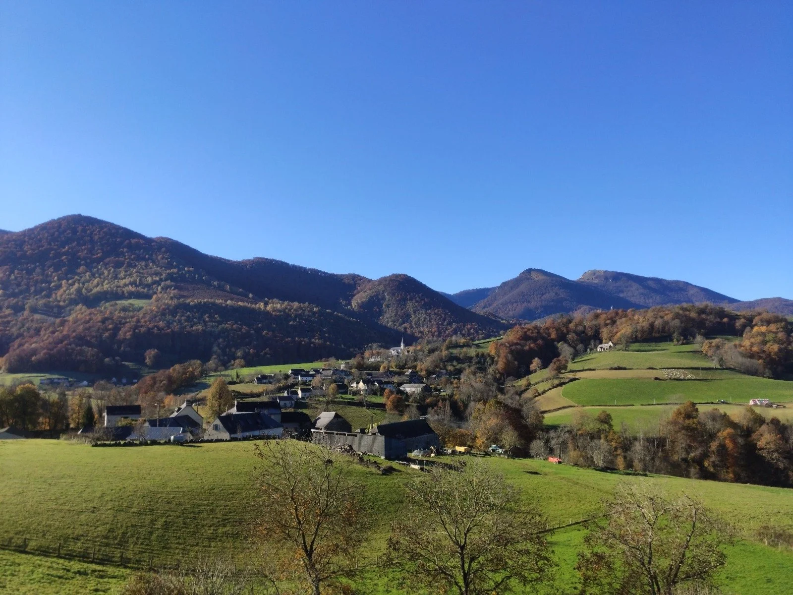 Paysage de montagnes avec un village, des collines verdoyantes et un ciel bleu clair.