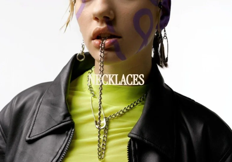Close-up of a woman with purple face paint, wearing a leather jacket, neon yellow shirt, and layered chain necklaces, with a chain in her mouth and overlaid writing saying 'NECKLACES'.