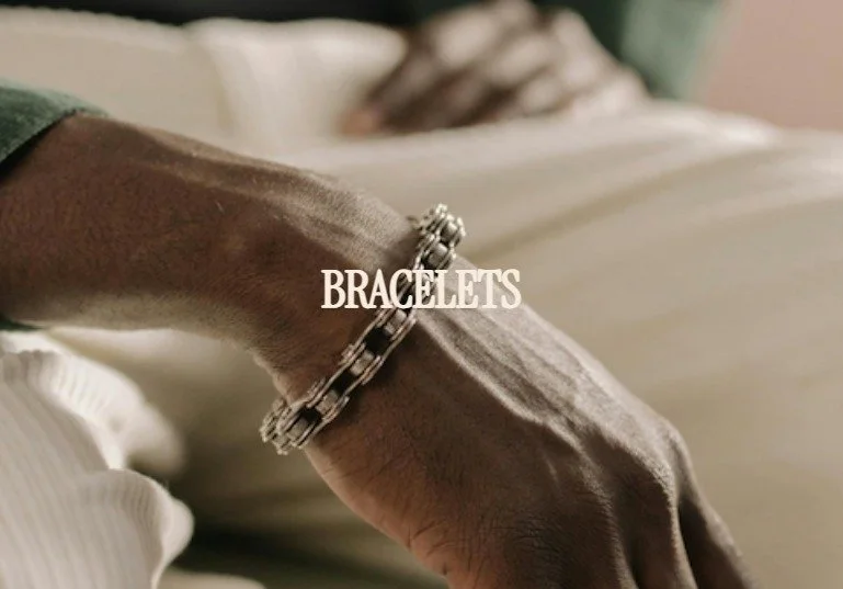 Close-up of a wrist wearing a silver bracelet with the word "BRACELETS" written over it, blurred background of a person sitting down.