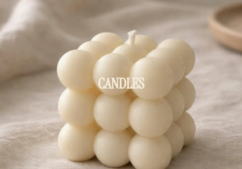 A decorative candle made of multiple small, white, spherical wax balls assembled in a cube shape with the word 'CANDLES' overlaid.