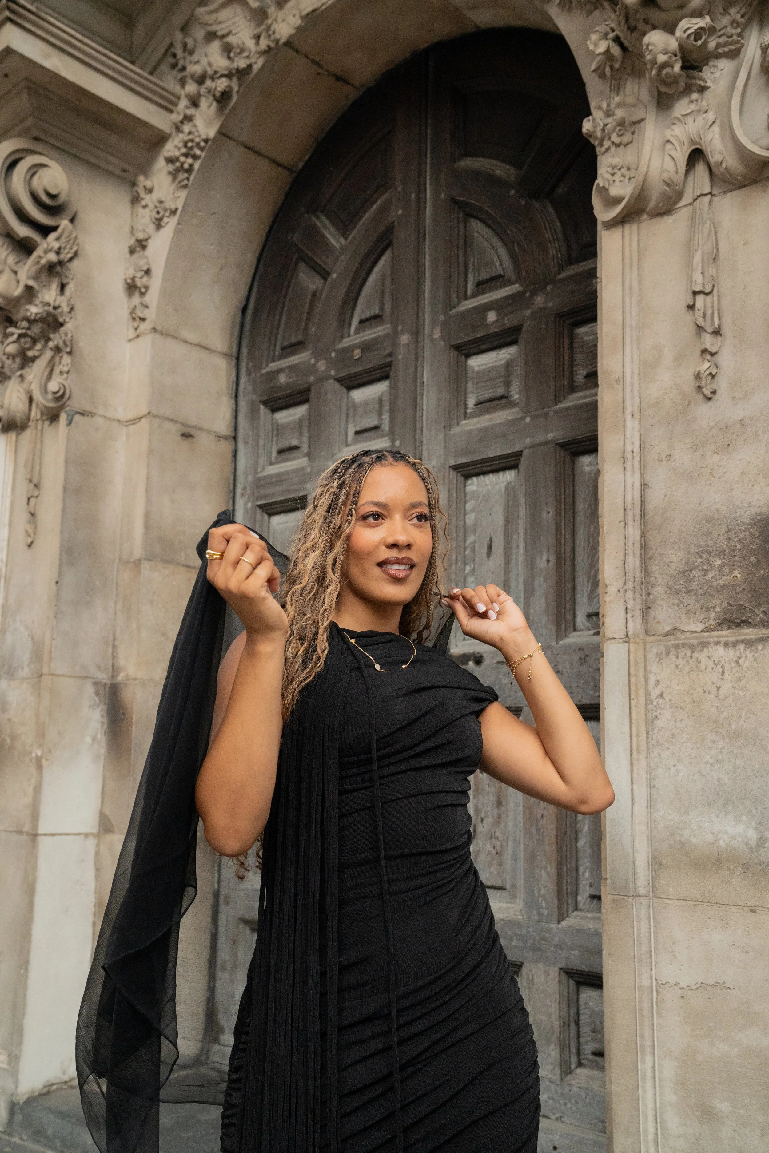 A woman with jewellery from Onna London posing in front of a large, ornate wooden door with detailed stone carvings on the archway surrounding it.