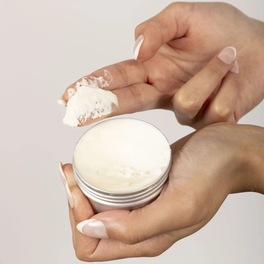 Person holding a jar of white cream from Dewy Skin and using a finger to scoop out some of the cream.