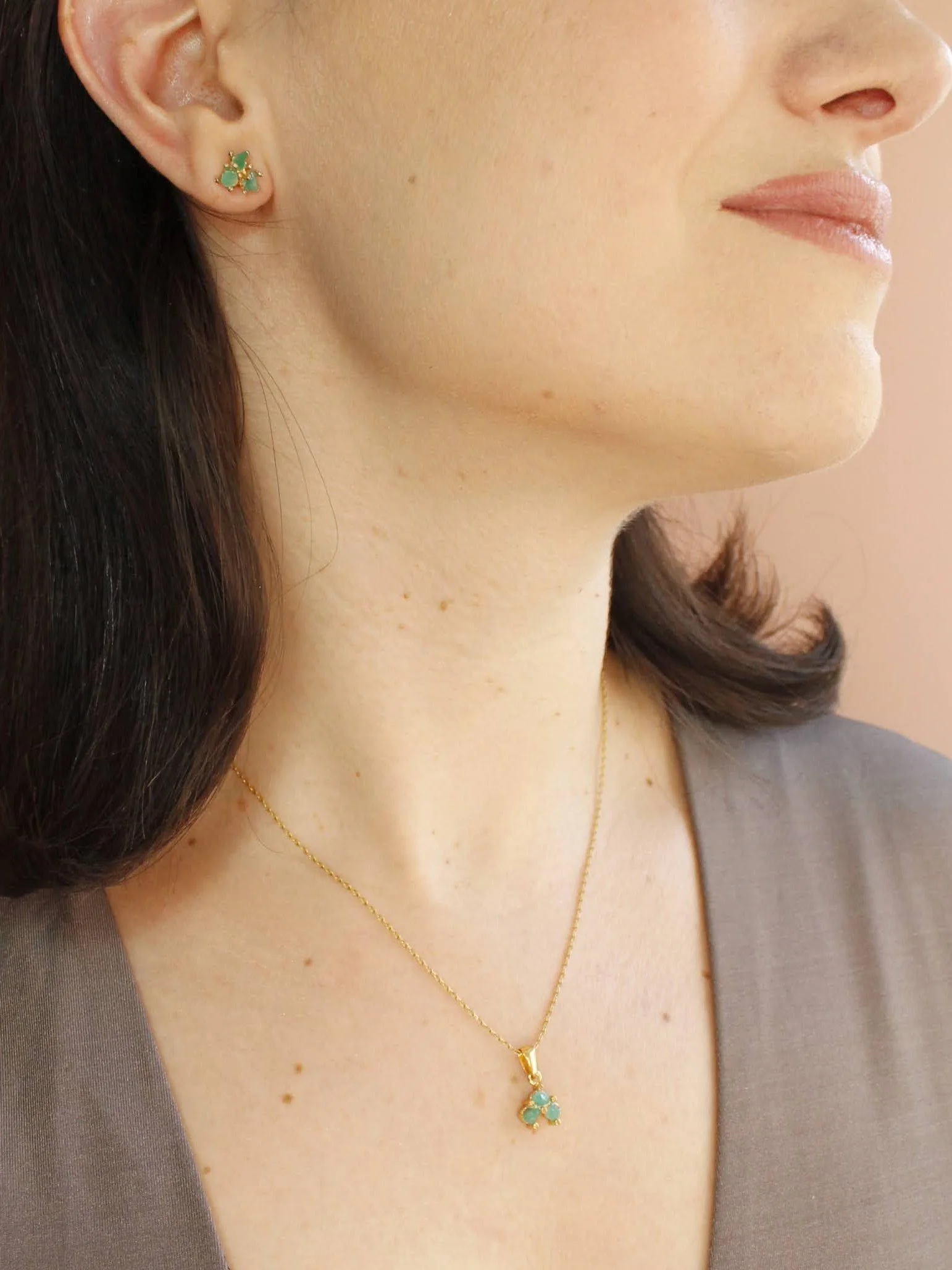 Close-up of a woman’s face, ear, and neck, showing emerald teal earrings and a matching pendant necklace with gold chains.