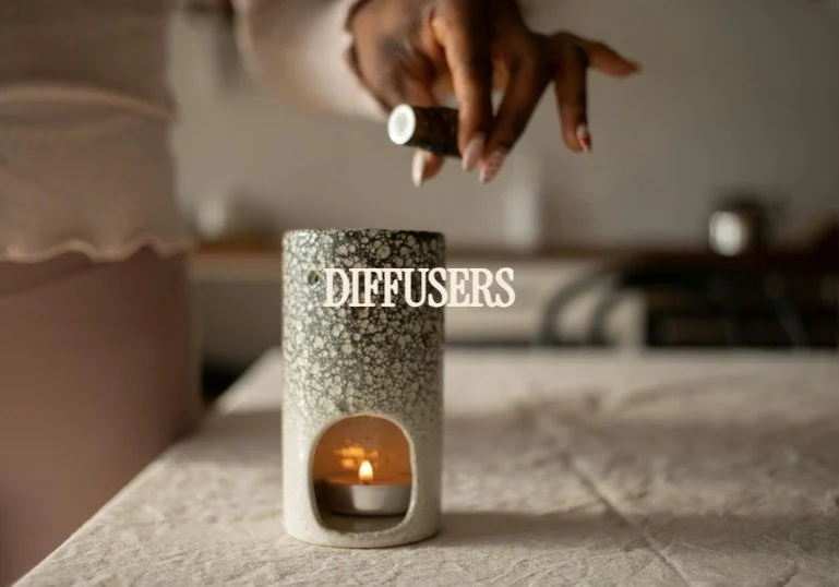 Close-up of a hand holding a diffuser bottle over a candle holder on a table, with the word 'DIFFUSERS' visible on the diffuser.