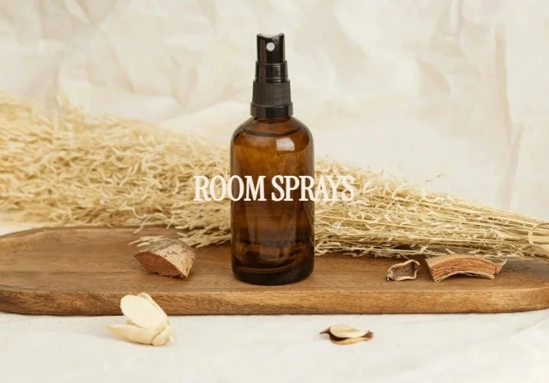 Amber glass spray bottle labeled 'Room Sprays' on a wooden surface surrounded by dried plants and cinnamon sticks.