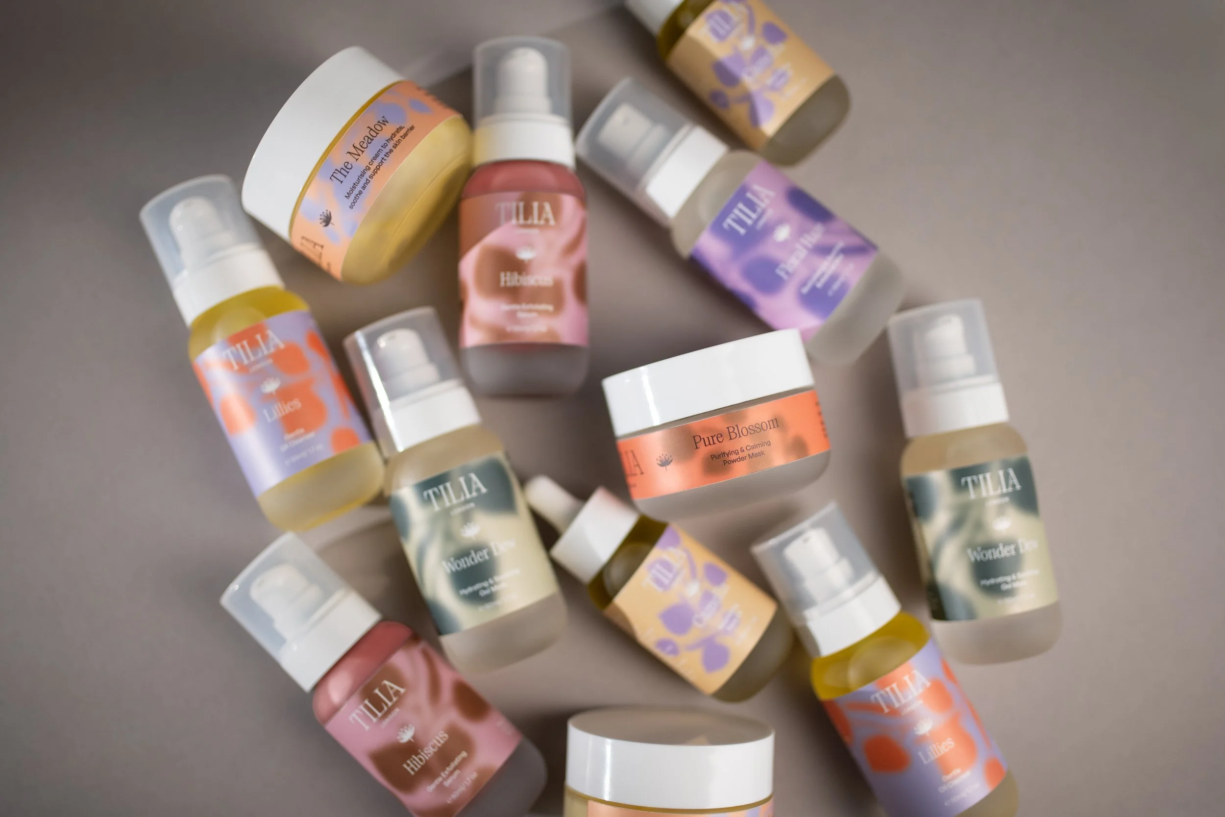 Assorted Tilia London skincare products, including bottles and jars with pastel-colored labels, arranged on a neutral surface.