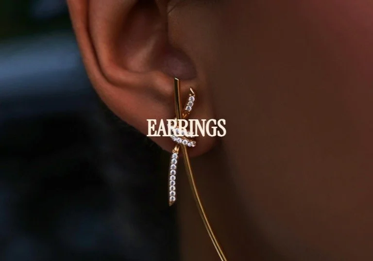 Close-up of a person's ear wearing a gold earring with embedded gems, with the word EARRINGS overlaid.