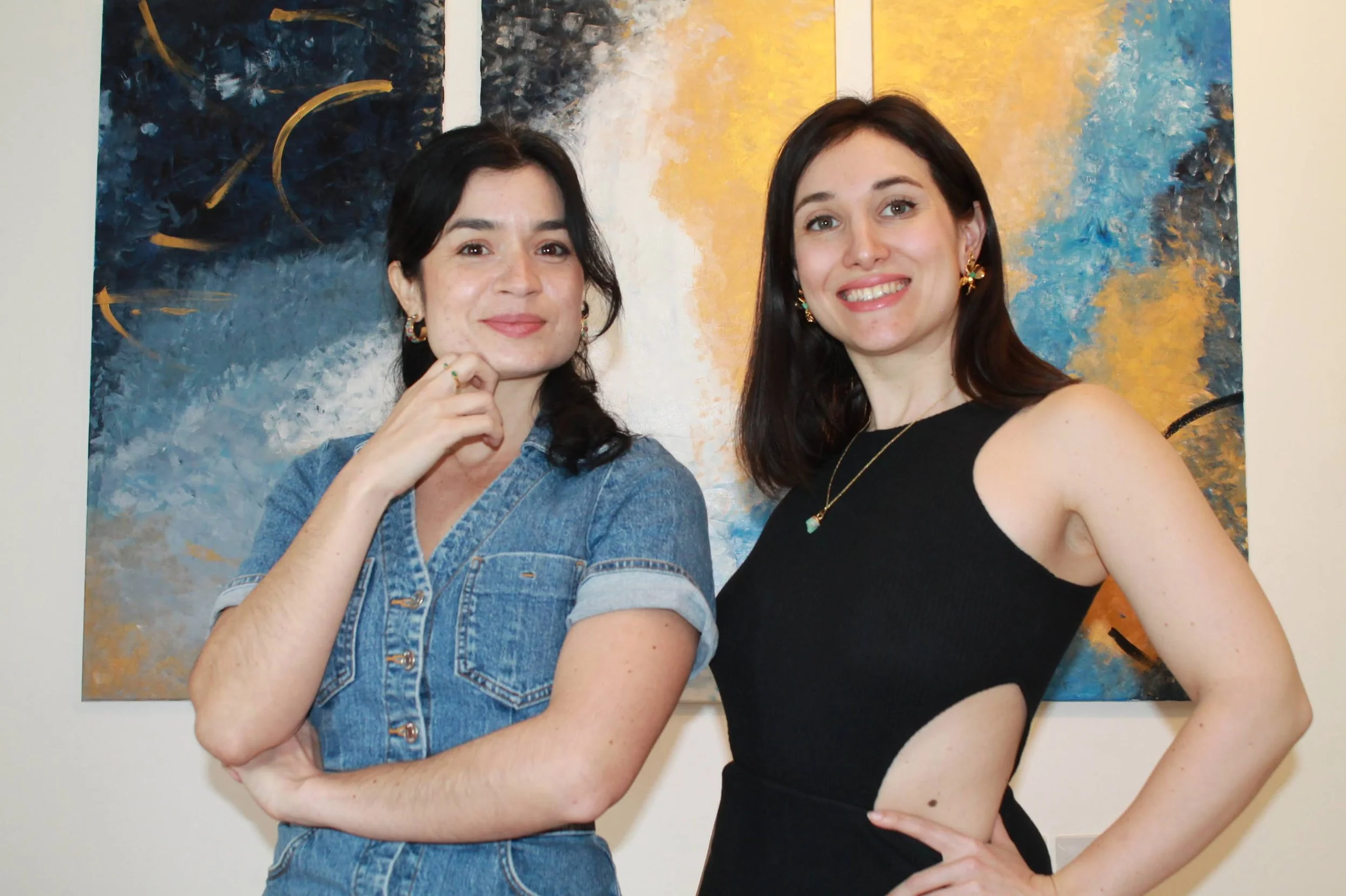 Two women standing side by side, smiling in front of an abstract painting with blue, yellow, and white colors, women are the founders of Mocana