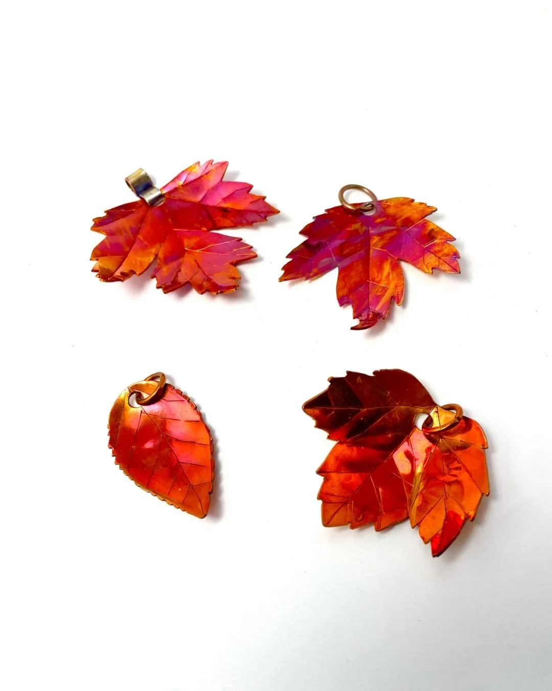 Four colorful leaf-shaped pendants with metal loops on a white background.
