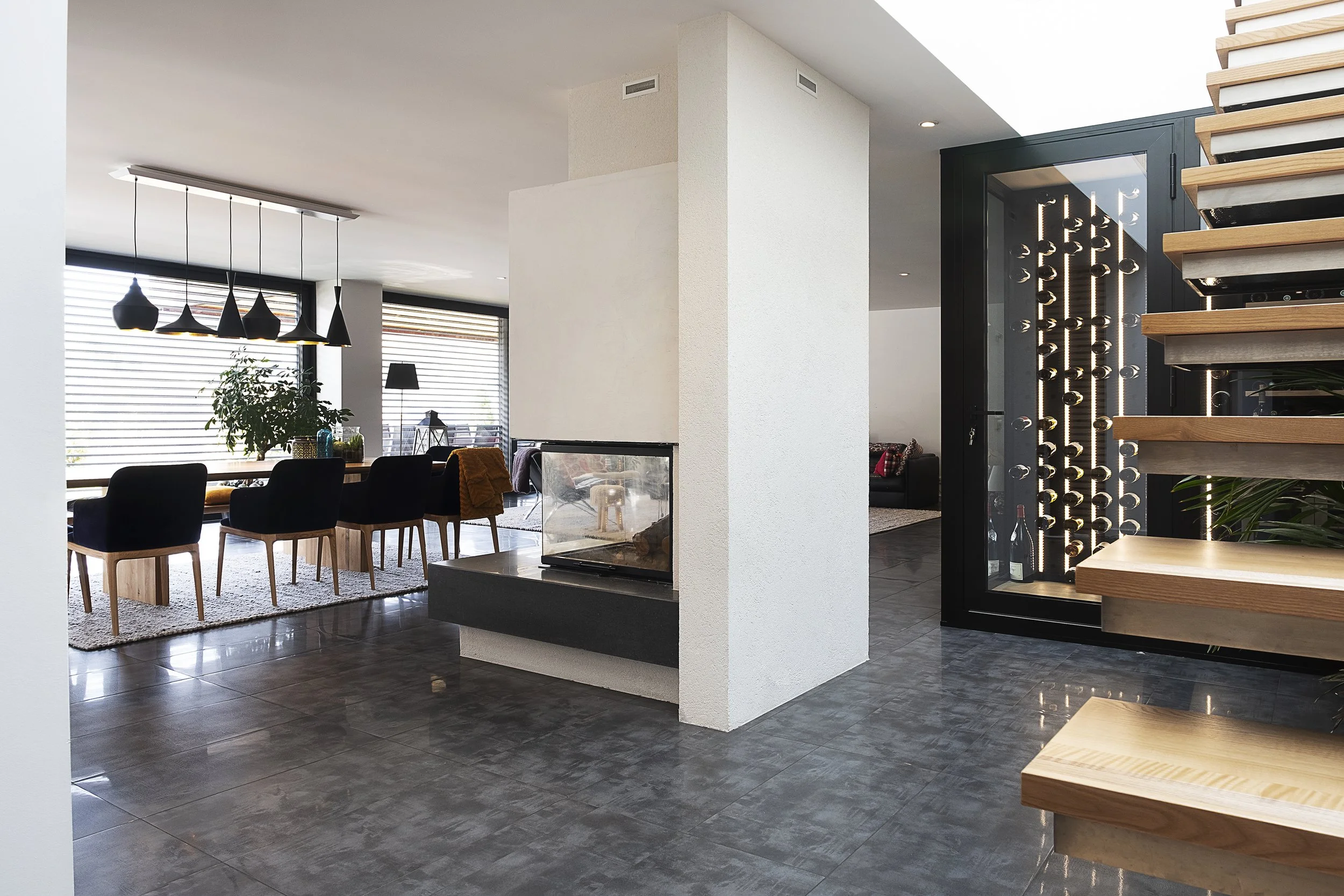 Intérieur moderne avec un coin repas, un mur avec cheminée, une cave à vin intégrée, et des escaliers en bois.