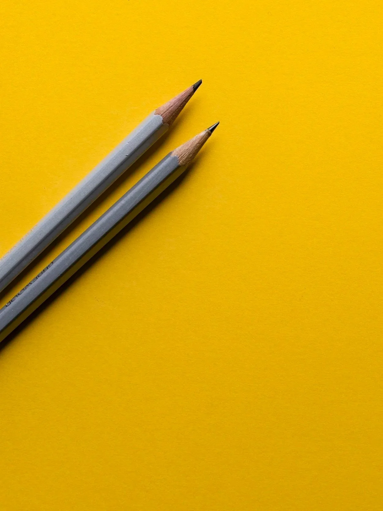 Two gray pencils with sharp tips on a yellow background.