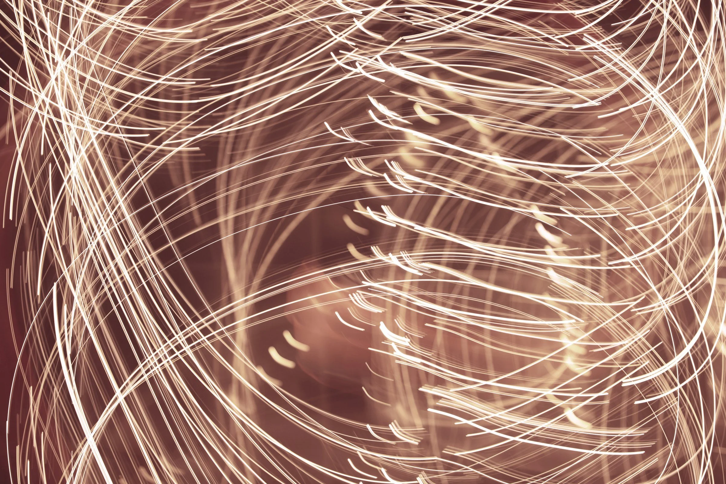 Light trails created by sparklers with streaks of warm, glowing light moving in various directions.