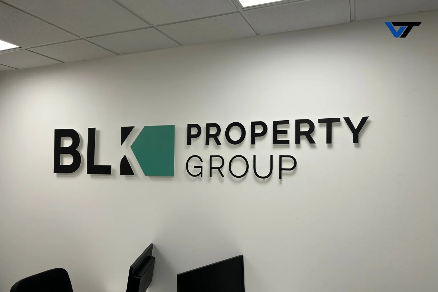 Sign on office wall that reads 'BLK Property Group' with a logo featuring a teal polygon and black and white text.