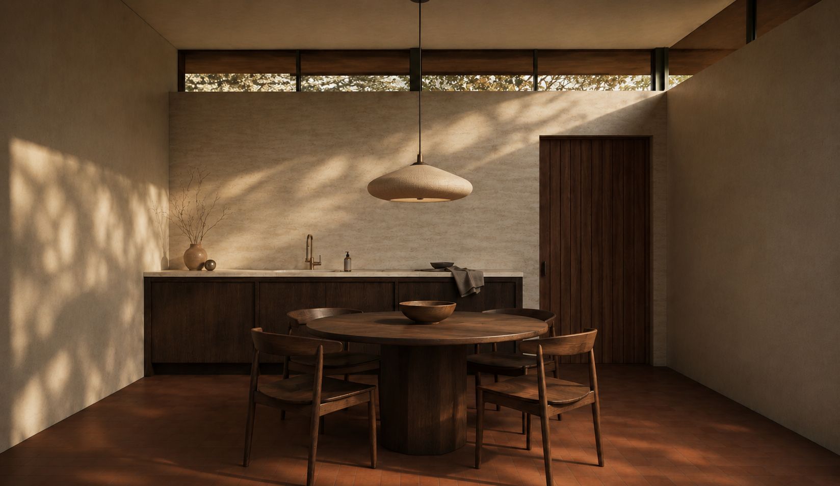 Minimalist kitchen with round wooden dining table and four chairs, dark wood cabinetry, beige walls, wooden door, large window at the top, pendant light, and warm sunlight casting shadows.