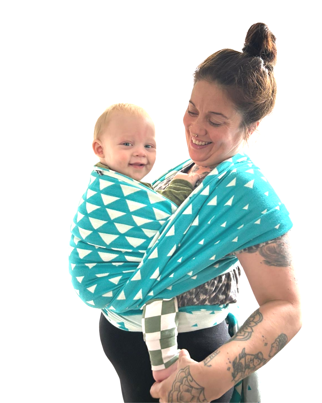 Woman with tattoos smiling while holding a young child in a blue and white patterned baby wrap, against a plain white background.
