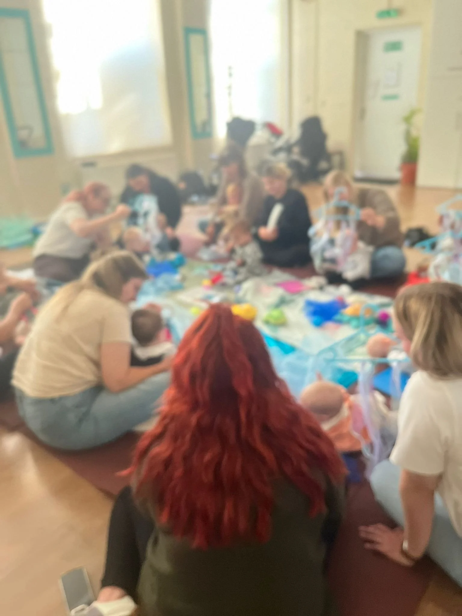 A group of women and children sitting on the floor and engaged in arts and crafts activities in a brightly lit room.