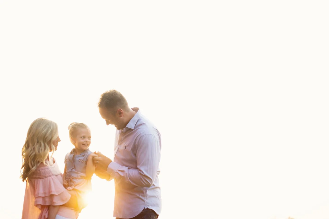 A man holding the hands of a young girl and woman, all smiling, with a bright background.